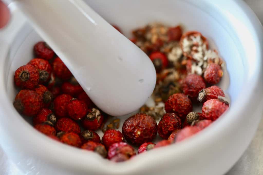 crushing dried rose hips with a mortar and pestle