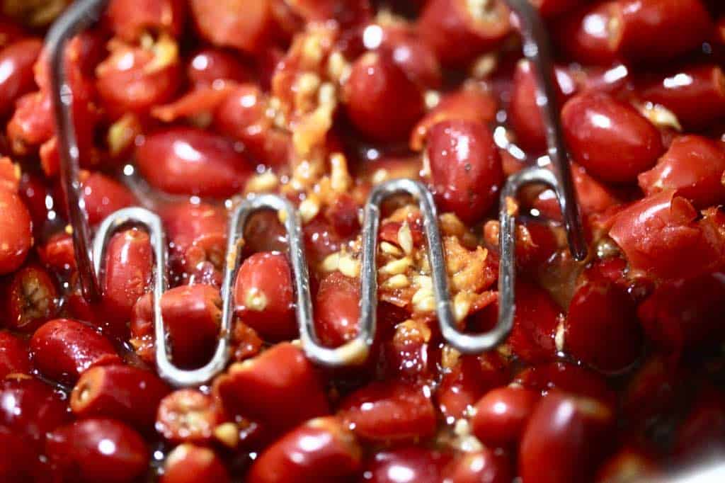 mashing rose hips in the pot to break up the whole pieces when they have softened