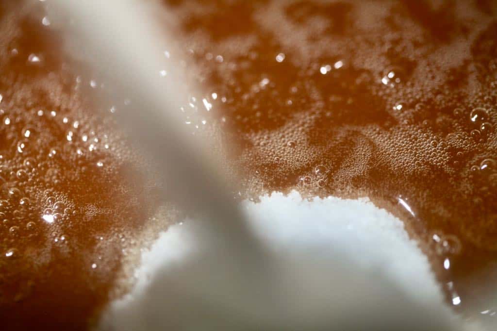 adding sugar to rose hip juice in a pot