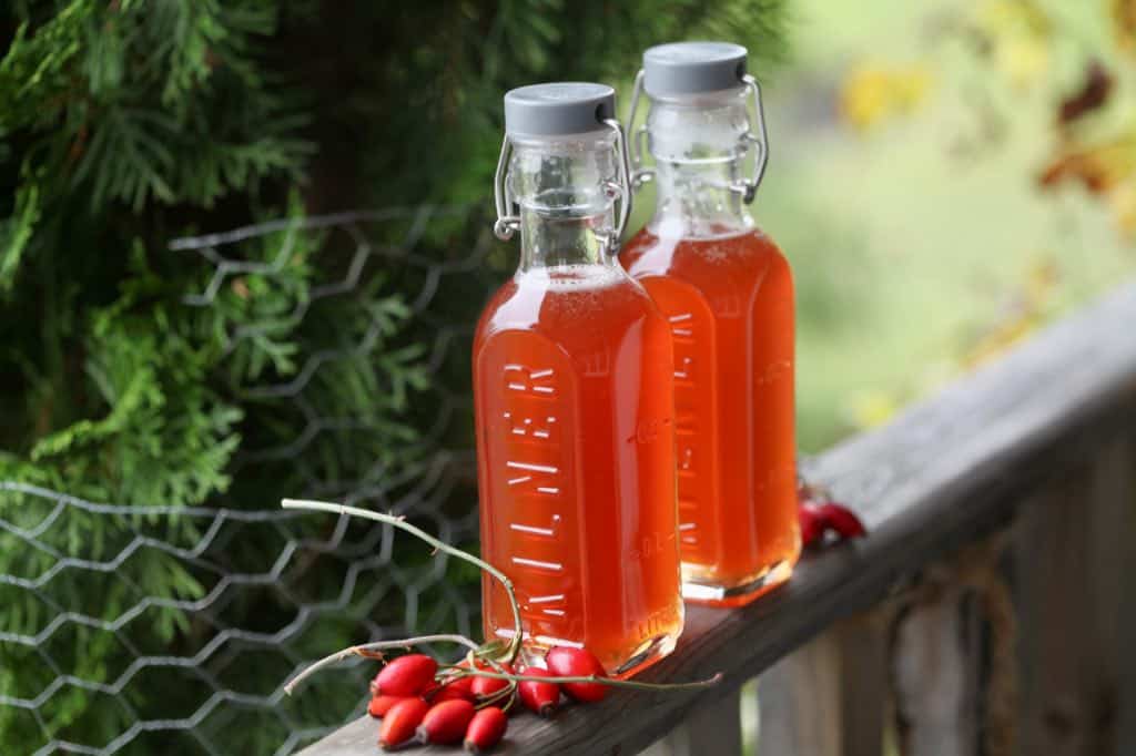 two bottles of rose hip syrup made from a  traditional recipe on a wooden railing,