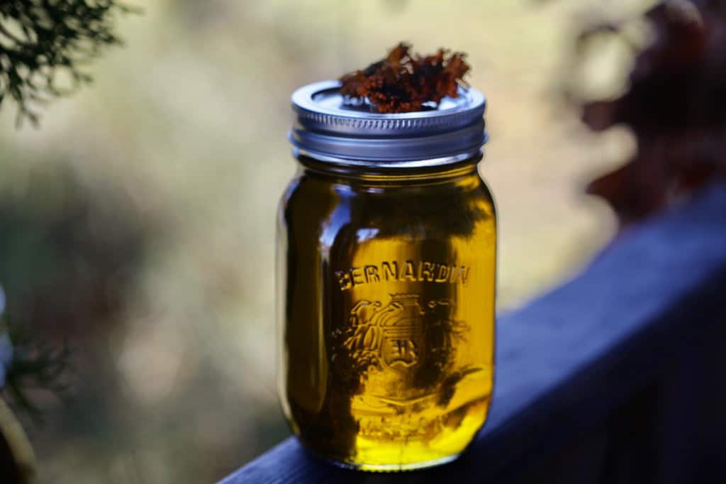 a mason jar full of calendula oil on a wooden railing