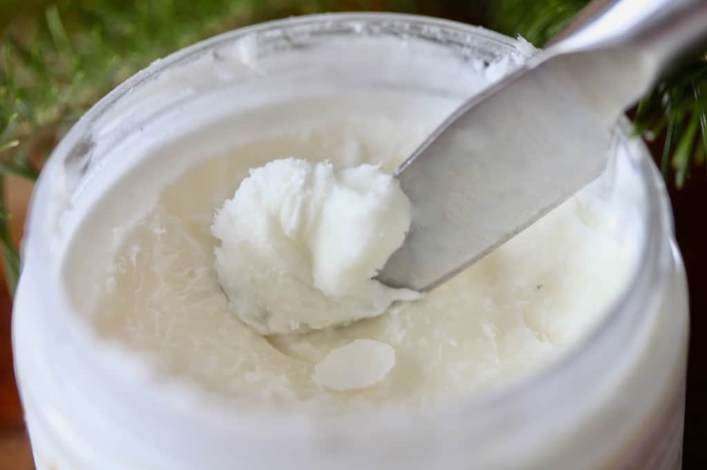 a container of shea butter, with a knife scraping a small amount out of the jar
