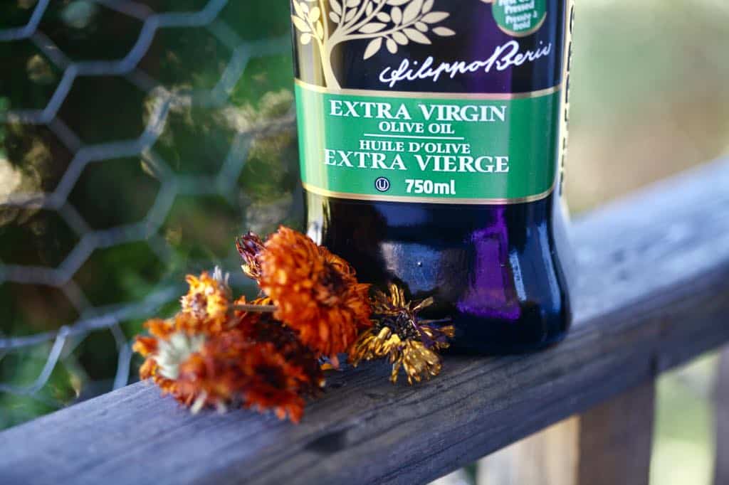 olive oil and dried calendula flowers on a wooden railing