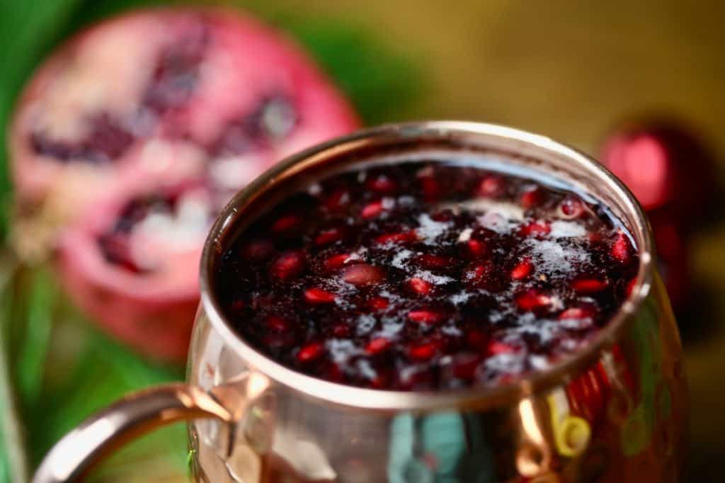 a copper mug with holiday mule in front of a blurred pomegranate and red ball Christmas decoration