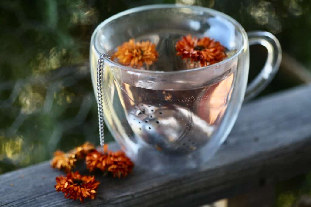 a clear glass cup of calendula tea on a wooden railing next to dried calendula flowers