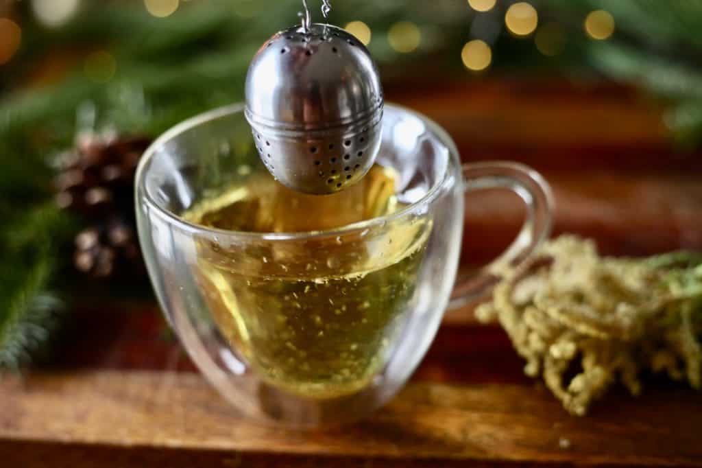 goldenrod tea in a glass cup next to a metal tea ball