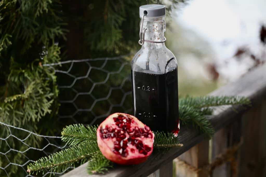 pomegranate simple syrup in a glass bottle on a wooden railing, next to a pomegranate half