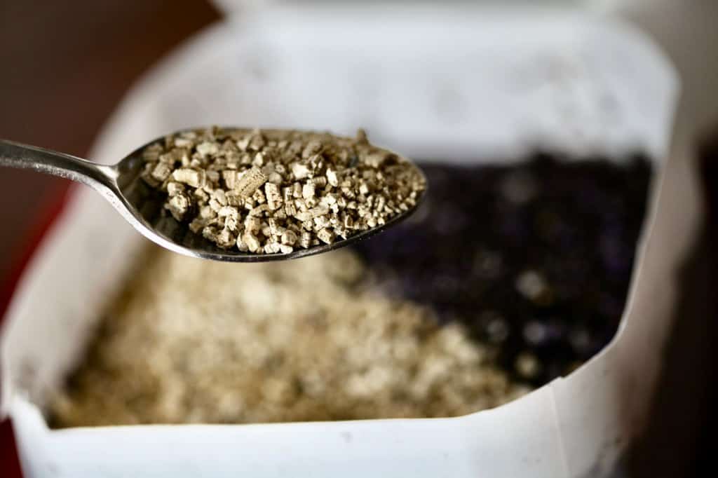a spoon full of vermiculite with a container of soil in the background