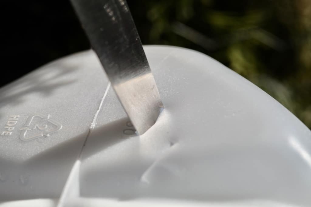 creating drainage holes in the bottom of a milk jug container with a sharp knife
