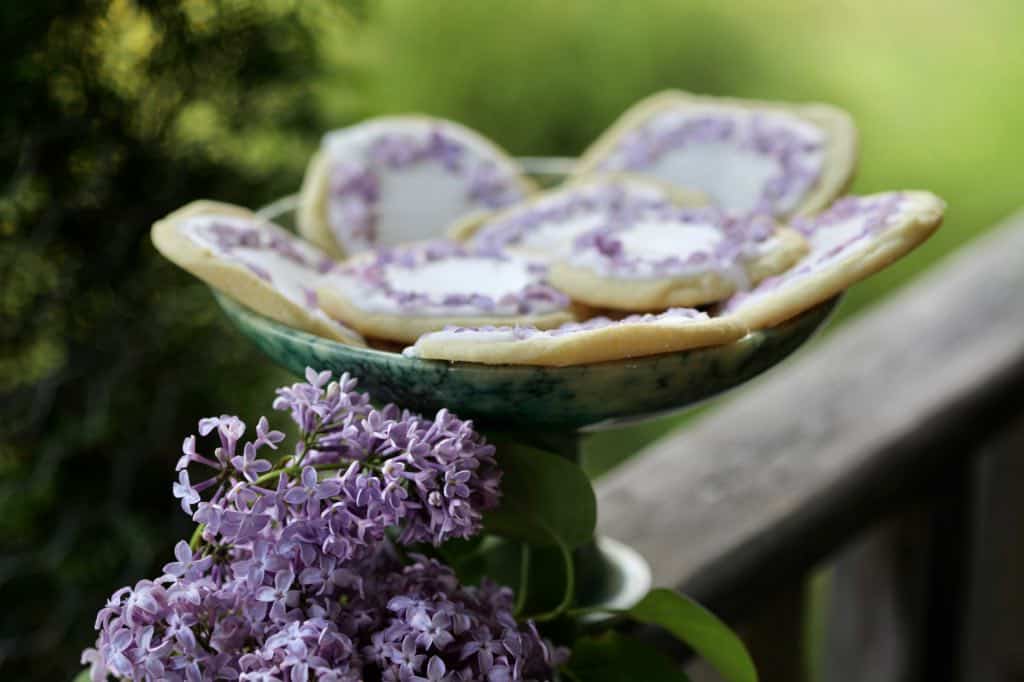 cookies on a green platter decorated with lilac blossoms, next to several fresh lilac flowers