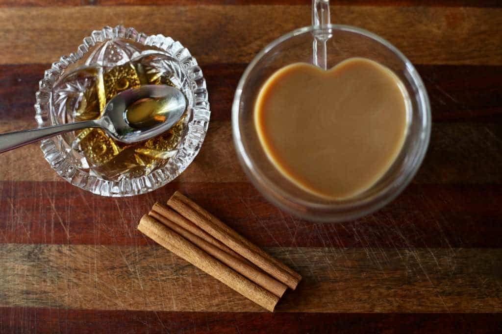 chicory tea in a heart shaped mug with cinnamon sticks and maple syrup on the surface beside the mug