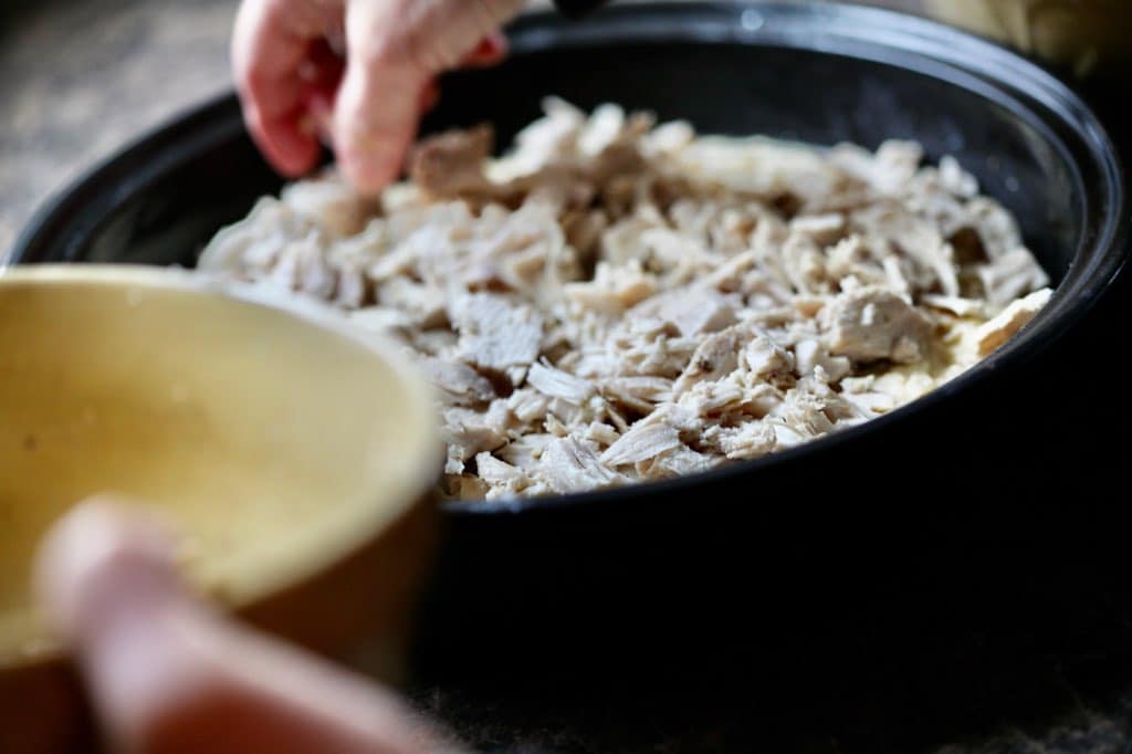 adding a layer of cubed chicken into a black cooking dish